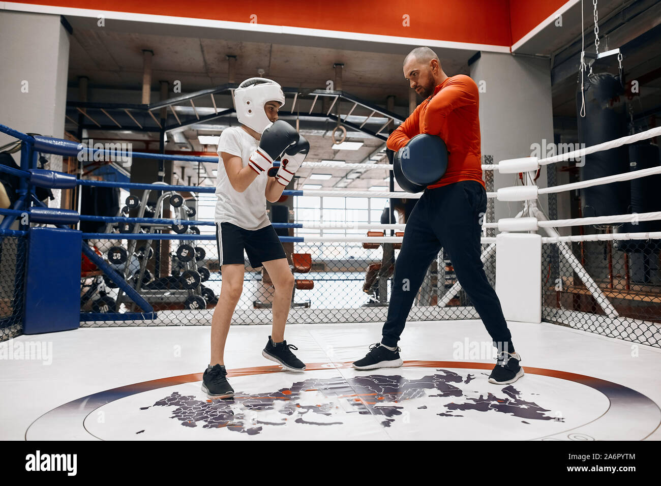 Poco boxer di T-shirt bianco. pantaloncini neri, casco, guanti di formazione con il suo papà. a piena lunghezza foto, boxe per begginers, programma unicue Foto Stock