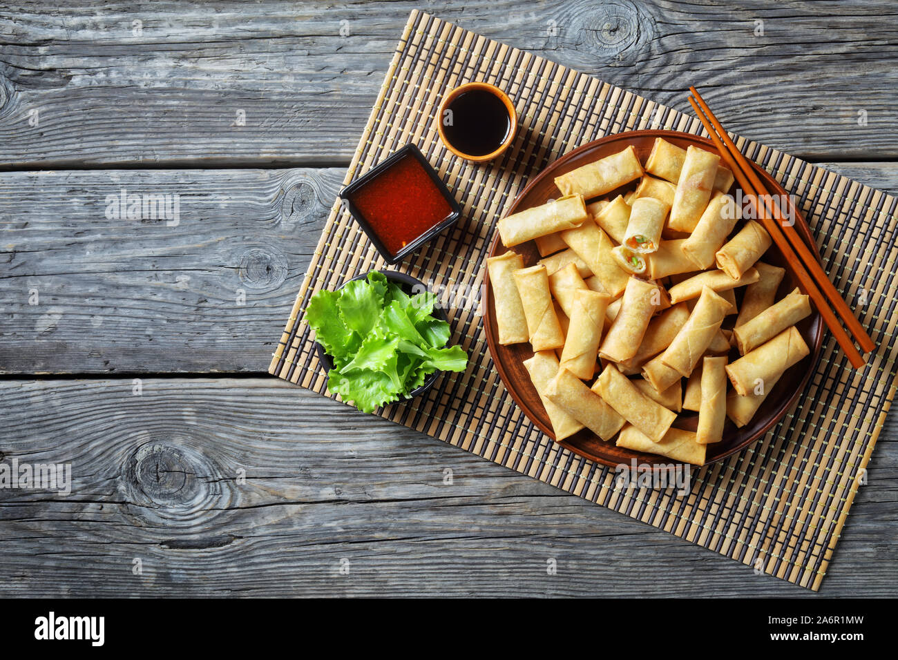 Fritte croccanti di morso dimensioni cinese involtini primavera con verze, carote e piselli verdi ripieni su una piastra su una tavola in legno rustico con salse, vista Foto Stock