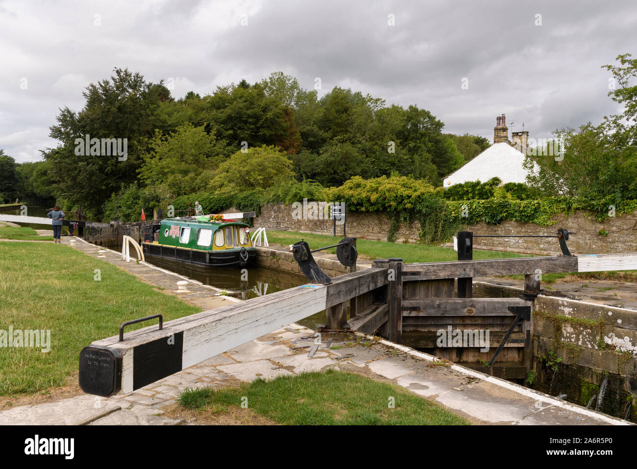 Narrowboat (stretta) barca vela su scenic rural Leeds Liverpool Canal passando attraverso il dispositivo di bloccaggio (persone da cancelli) - Gargrave, North Yorkshire, Inghilterra, Regno Unito Foto Stock