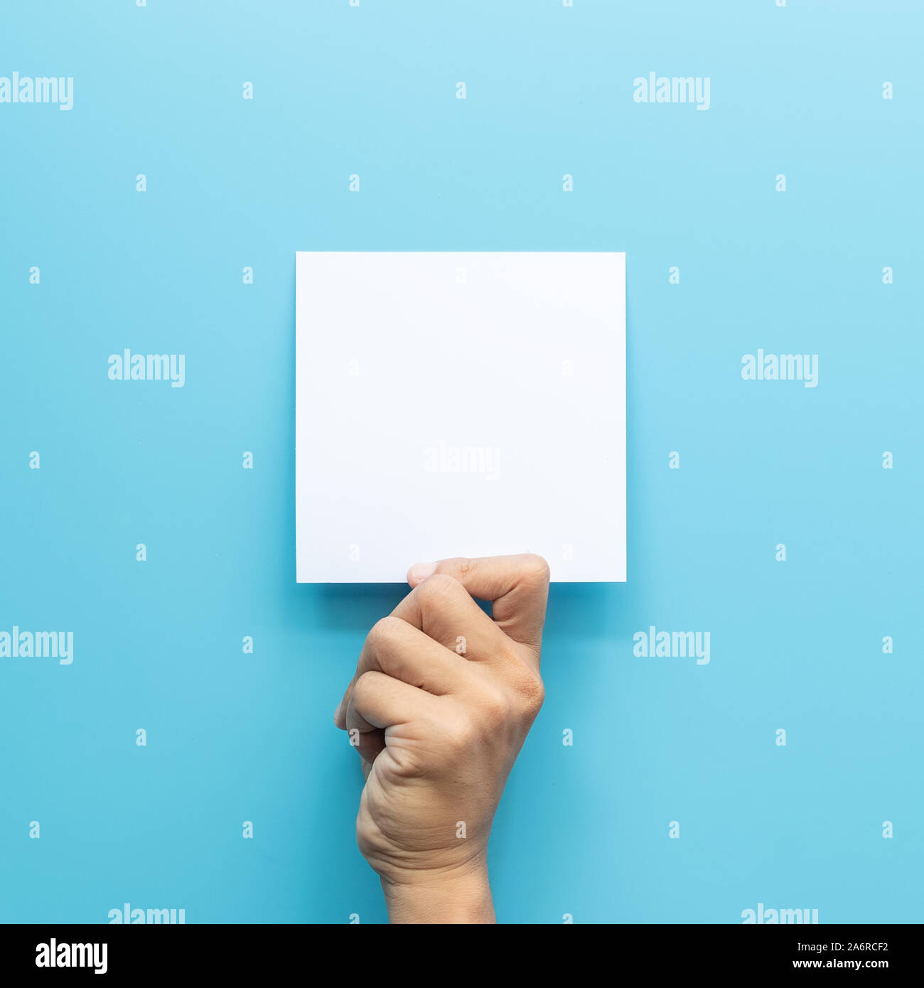 Man mano che tiene la scheda vuota del foglio di carta isolato su sfondo blu con una copia dello spazio. Foto Stock