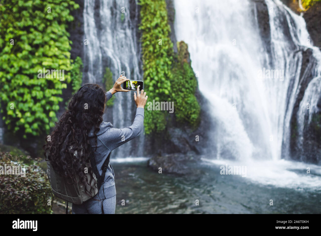 La donna sta immagine di cascata Banyumala in Bali. Lunga parentesi brunette capelli, zaino. Concetto di viaggio. Foto Stock