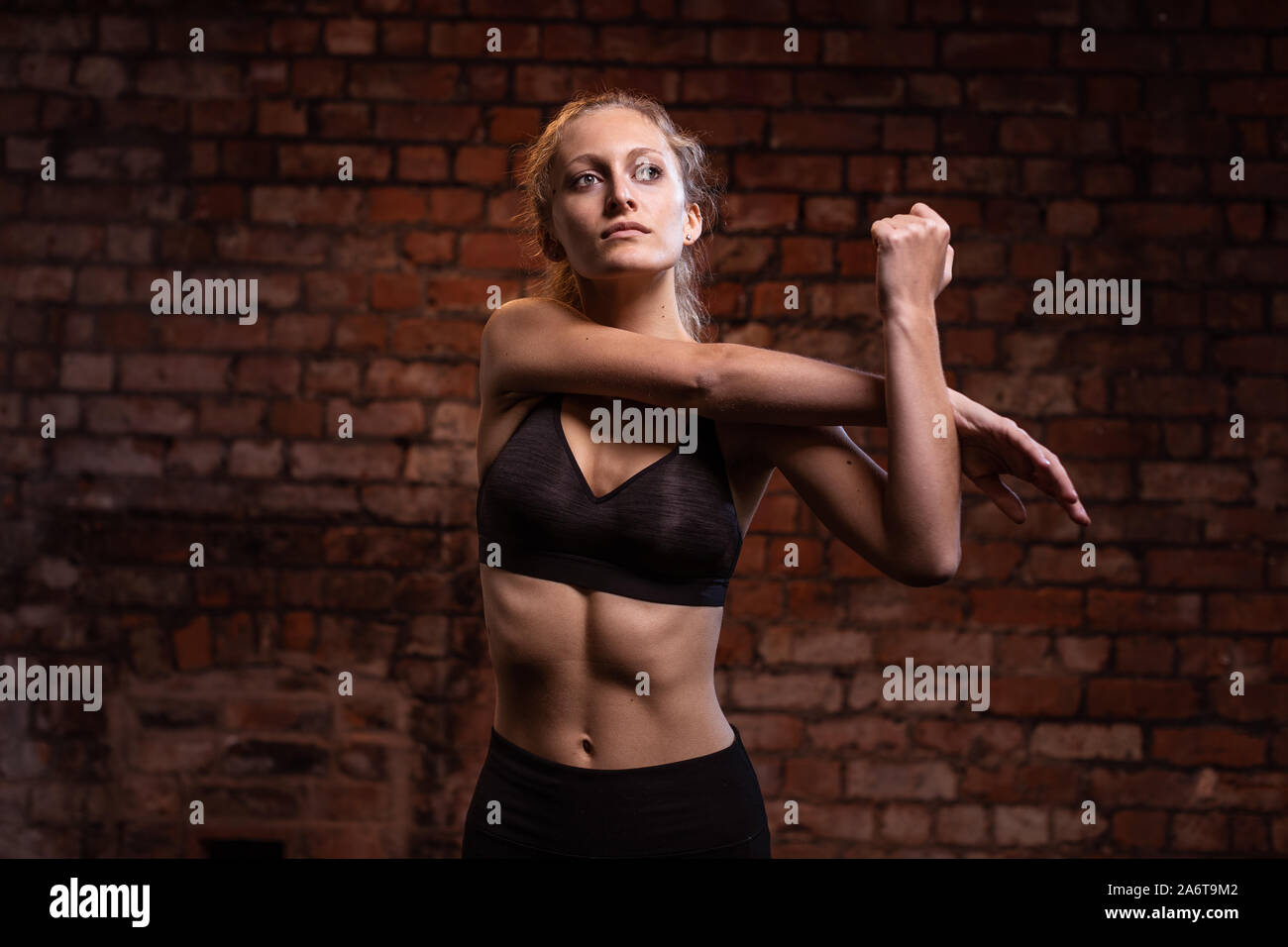 Un giovane, fiducioso athletic ragazza bionda con una coda di cavallo fa vari fitness pone di fronte un muro di mattoni, di notte. Foto Stock