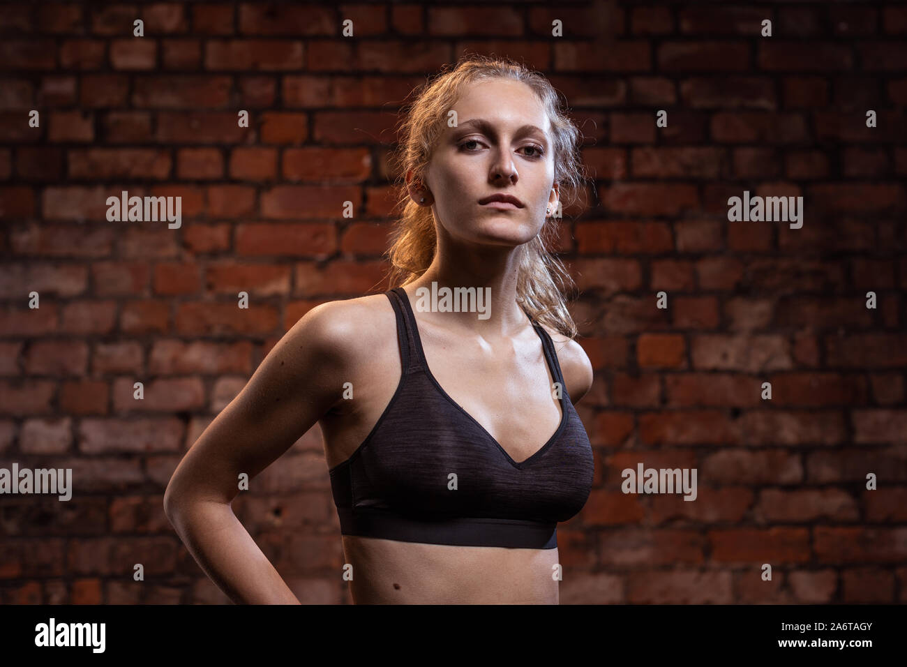 Un giovane, fiducioso athletic ragazza bionda con una coda di cavallo fa vari fitness pone di fronte un muro di mattoni, di notte. Foto Stock