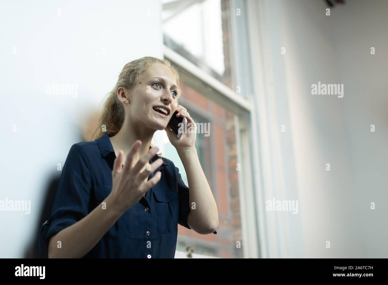 Un giovane, naturale cerca ragazza bionda con una coda di cavallo utilizza uno smartphone in un ambiente bianco Foto Stock