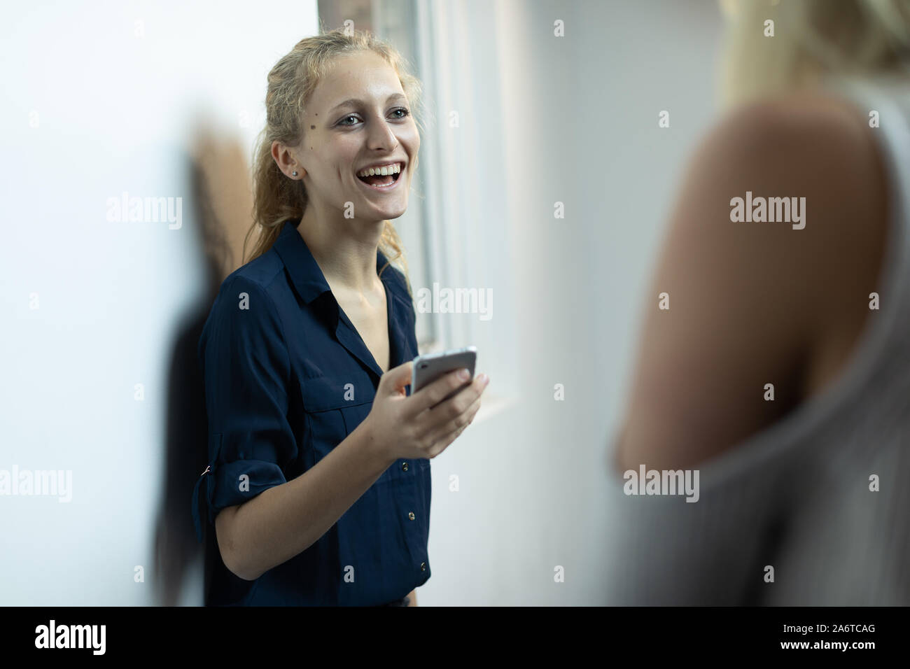 Un giovane, naturale cerca ragazza bionda con una coda di cavallo utilizza uno smartphone in un ambiente bianco Foto Stock