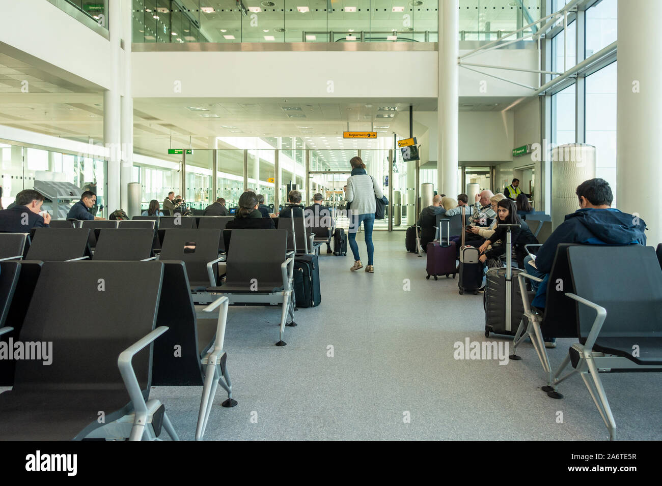 Persone sedersi sui sedili e attendere a un gate di partenze in aeroporto di Heathrow. Foto Stock