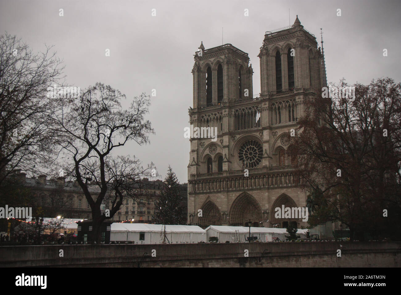 Vista laterale della cattedrale di Notre Dame, bianco bancarelle natalizie e alberi in Parvis square - giorno nuvoloso a Parigi, Francia - Verticale colpo di landmar principale Foto Stock