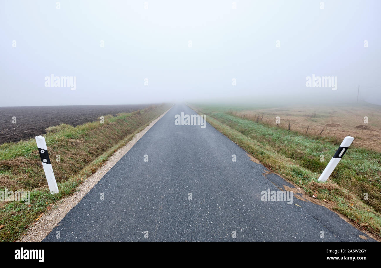 Strada di campagna in nessun luogo - narow street con diminuzione perspektive portando nella nebbia. Visto in Germania vicino Oedenberg, Baviera in ottobre. Foto Stock