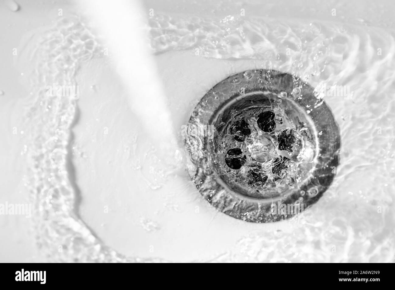 Un flusso di acqua pulita fluisce nel foro di scarico di un lavabo bianco con una profondità di campo ridotta Foto Stock