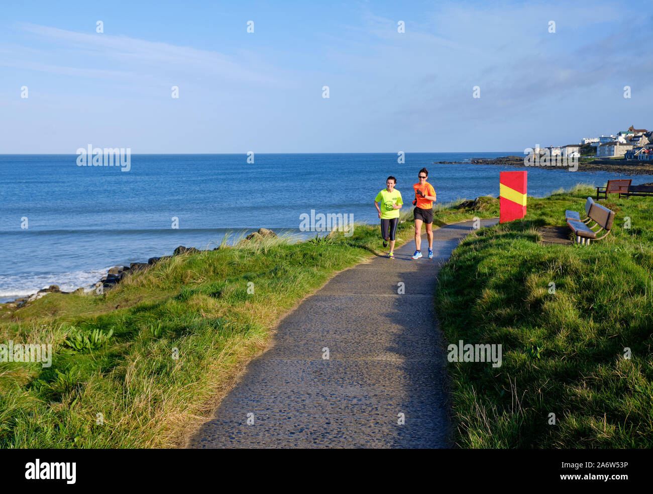 Due donne che corrono lungo il percorso costiero su un vivace mattina di sole in Portstewart Irlanda del Nord Foto Stock