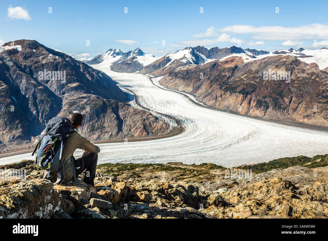 Uomo su backpacking trip escursionismo e trekking sui ghiacciai. Egli si trovi a poggiare su una roccia che si affaccia sul Ghiacciaio di salmone in remote Canadiam montagne vicino Foto Stock