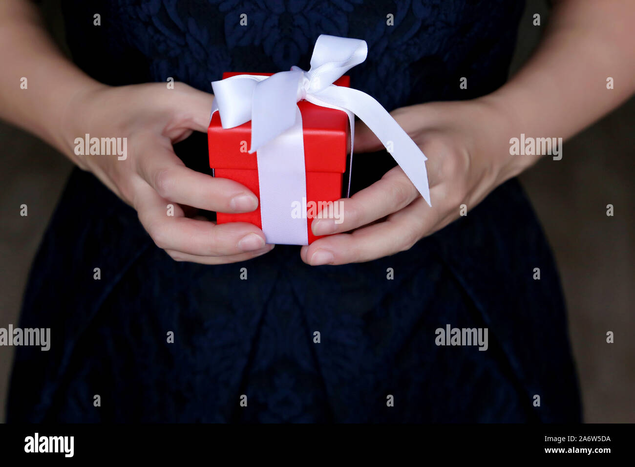 Confezione regalo rossa in mani femminili, donna in blu abito da sera tenendo presente. Concetto di sorpresa romantica, Natale e Capodanno Foto Stock
