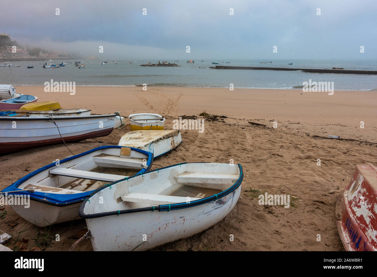 Barche su una spiaggia di sabbia in un nuvoloso, nebbioso giorno di Paço de Arcos vicino a Lisbona, Portogallo Foto Stock