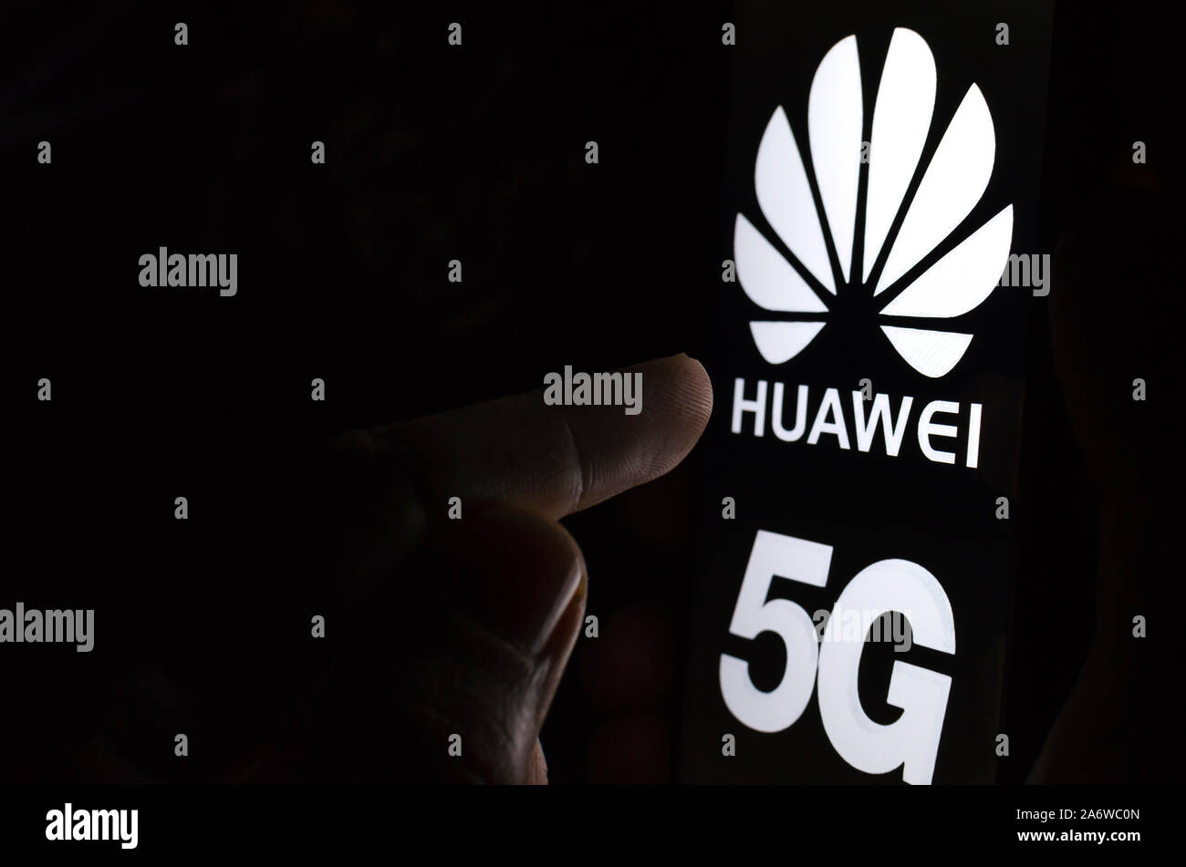 Huawei 5G logo su una schermata dello smartphone in una stanza buia e un dito di toccarlo. Foto Stock