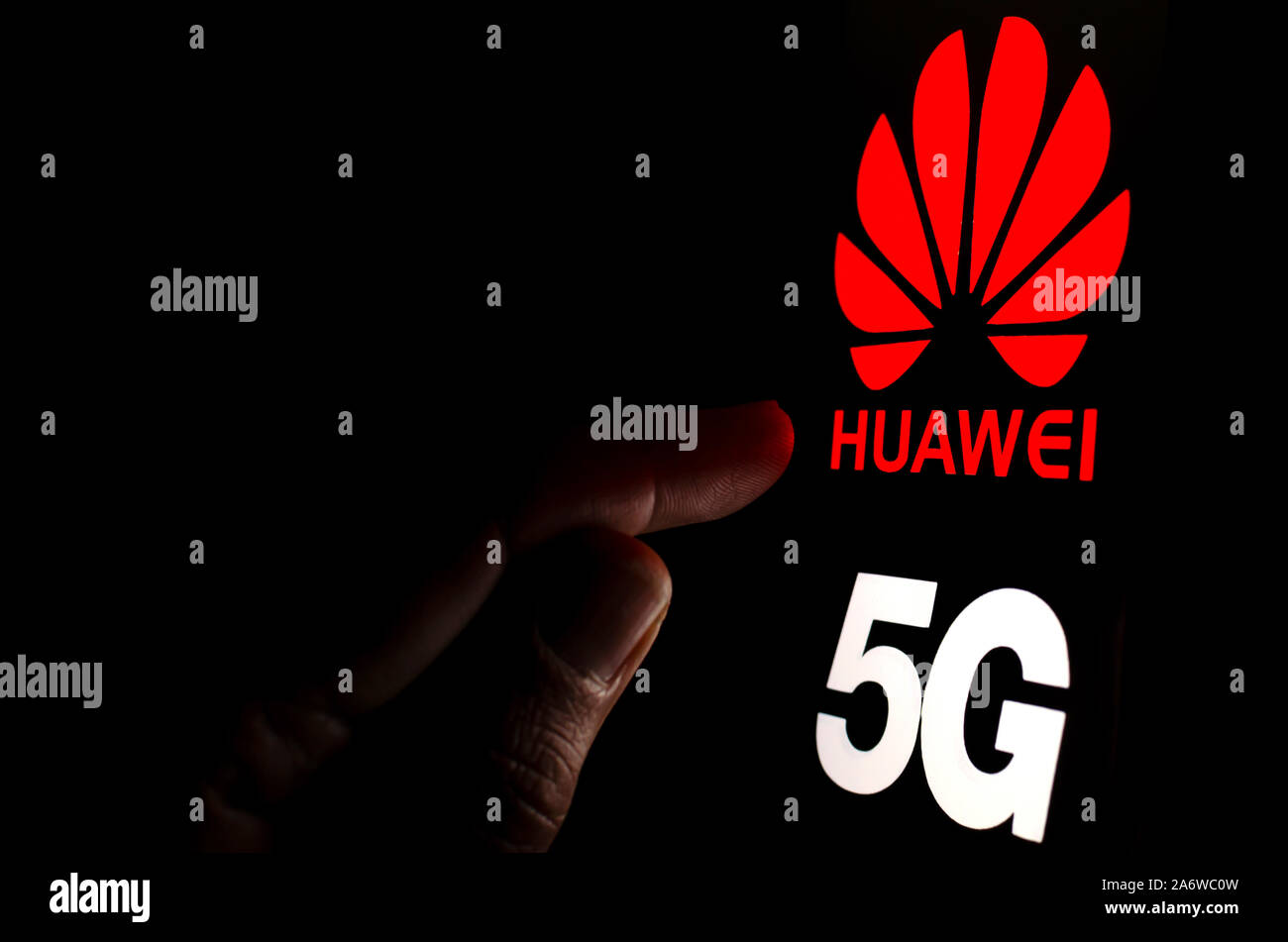 Huawei 5G logo su una schermata dello smartphone in una stanza buia e un dito di toccarlo. Foto Stock