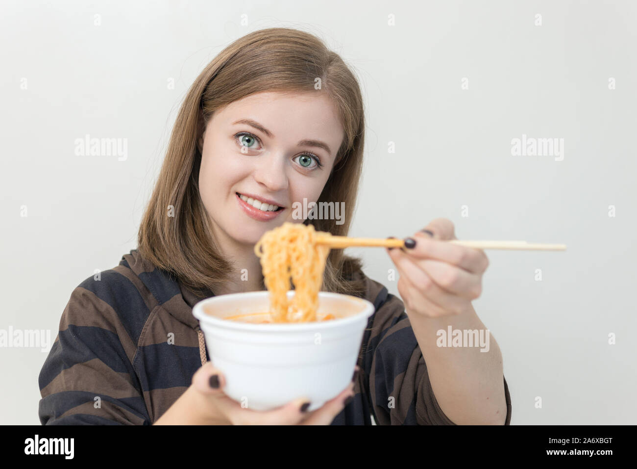 Giovane ragazza caucasica donna mangiare tagliatelle istante ramen con bacchette Foto Stock