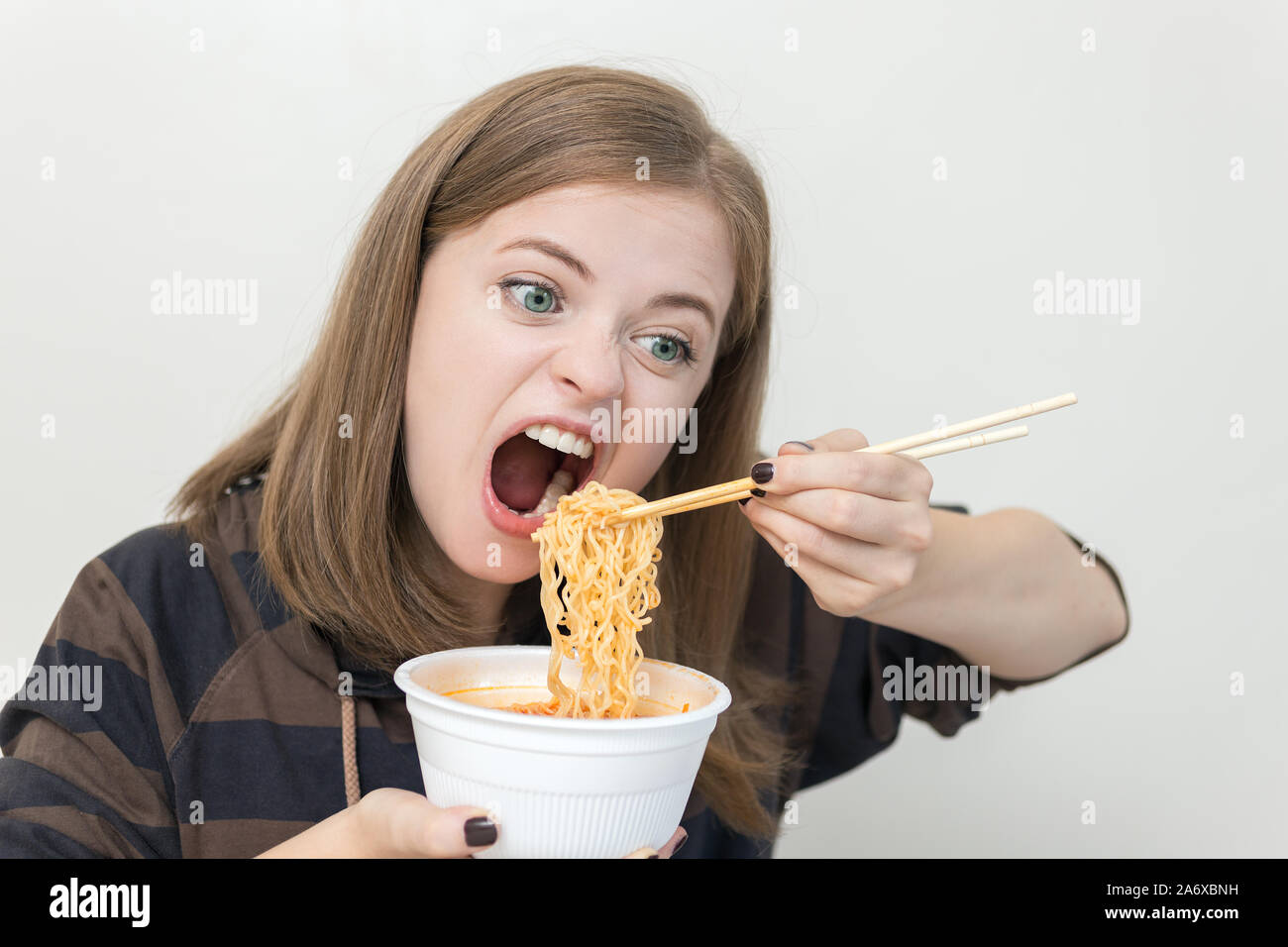 Giovane ragazza caucasica donna mangiare tagliatelle istante ramen con bacchette Foto Stock