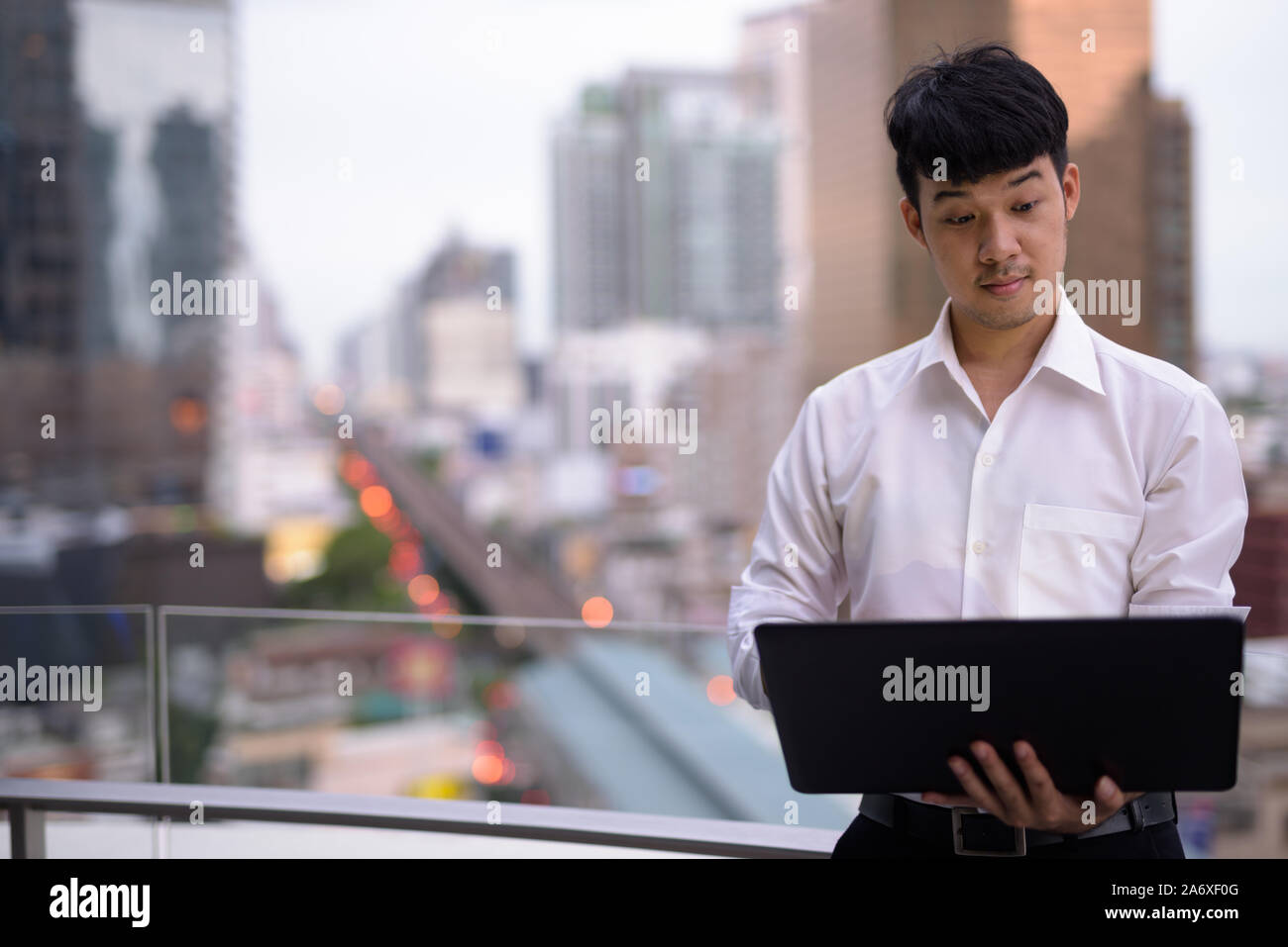 Ritratto di giovane imprenditore asiatici utilizzando laptop contro la vista della città Foto Stock