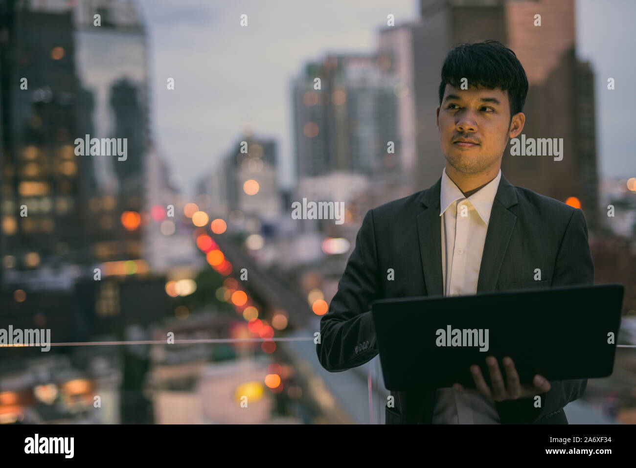 Ritratto di giovane imprenditore asiatici utilizzando laptop contro la vista della città Foto Stock