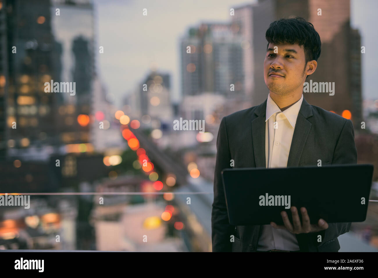 Ritratto di giovane imprenditore asiatici utilizzando laptop contro la vista della città Foto Stock