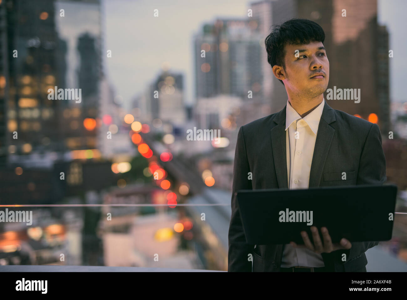 Ritratto di giovane imprenditore asiatici utilizzando laptop contro la vista della città Foto Stock