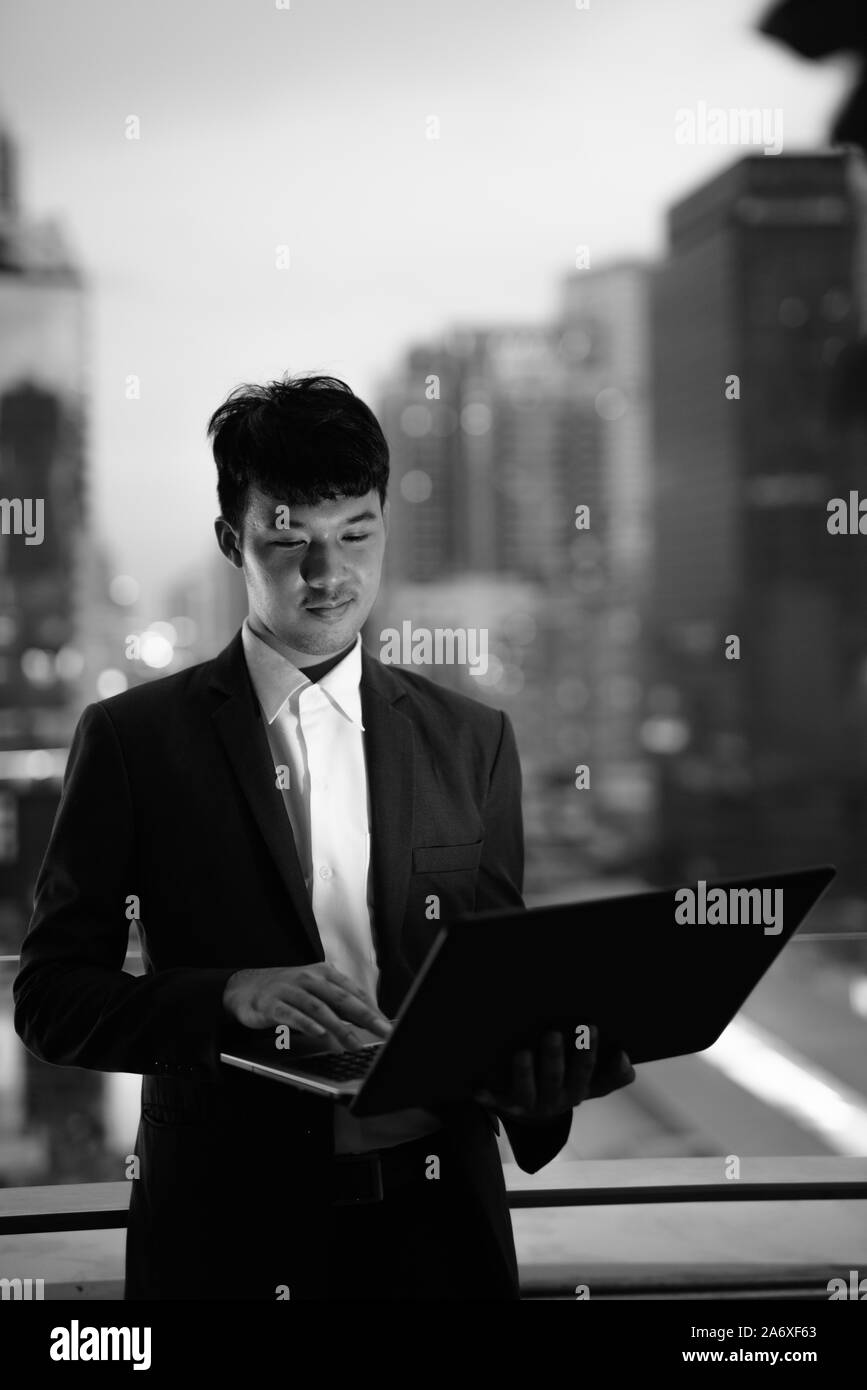 Ritratto di giovane imprenditore asiatici utilizzando laptop contro la vista della città Foto Stock