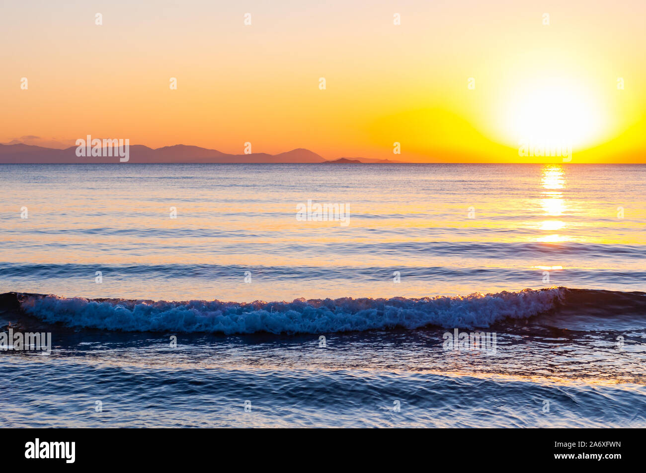 Il sole al tramonto sta andando verso il basso dietro l'orizzonte. Mar  Tirreno bay con isola d'Elba sullo sfondo al tramonto. Cala Violina,  Scarlino, Pr Foto stock - Alamy