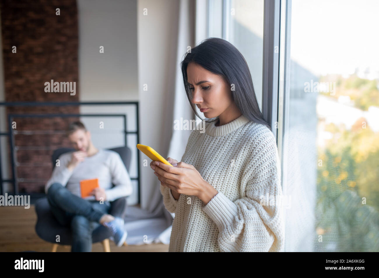 Moglie mentre tiene il suo smartphone durante la lettura dei messaggi Foto Stock