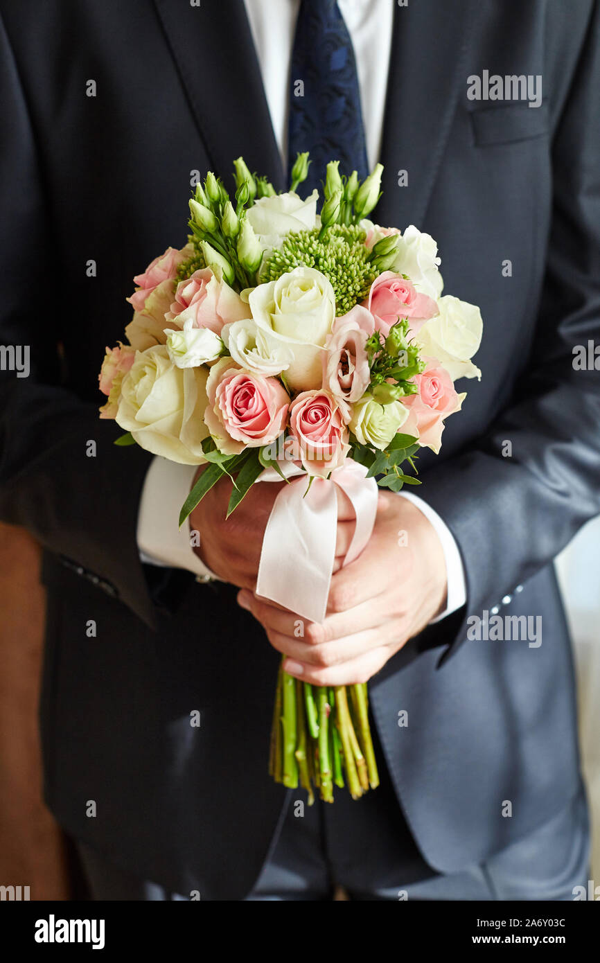 L'uomo sposo detiene il bouquet della sposa. Il govern incontra la sposa con un bouquet di fiori. Ragazzo in giacca e cravatta con un mazzo di rose nelle sue mani Foto Stock