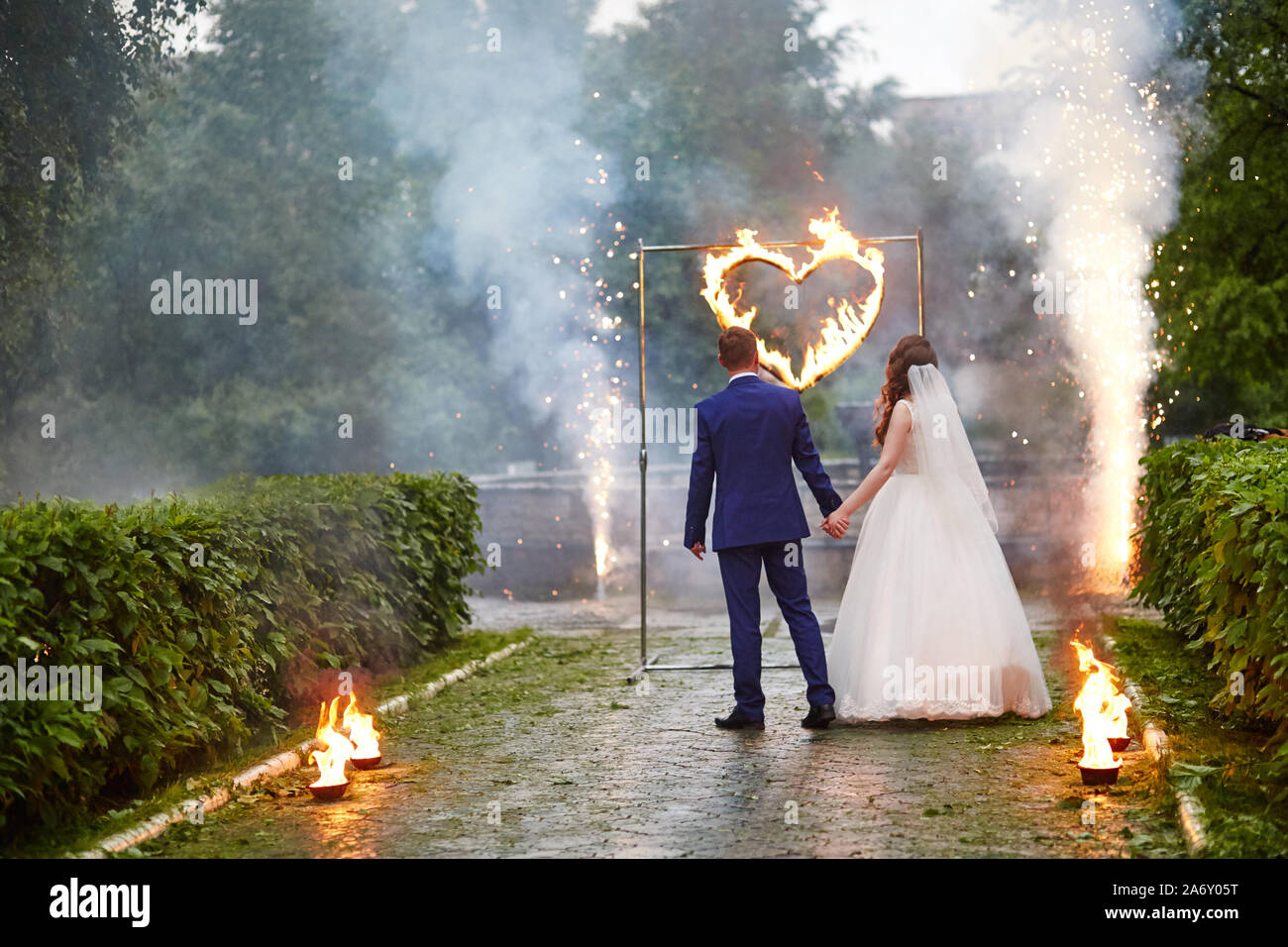 Sposa e lo sposo guardare il fire show. Cuore in fiamme e scintille nel fumo. Il completamento della cerimonia nuziale. Giovane trattenere reciprocamente le mani Foto Stock