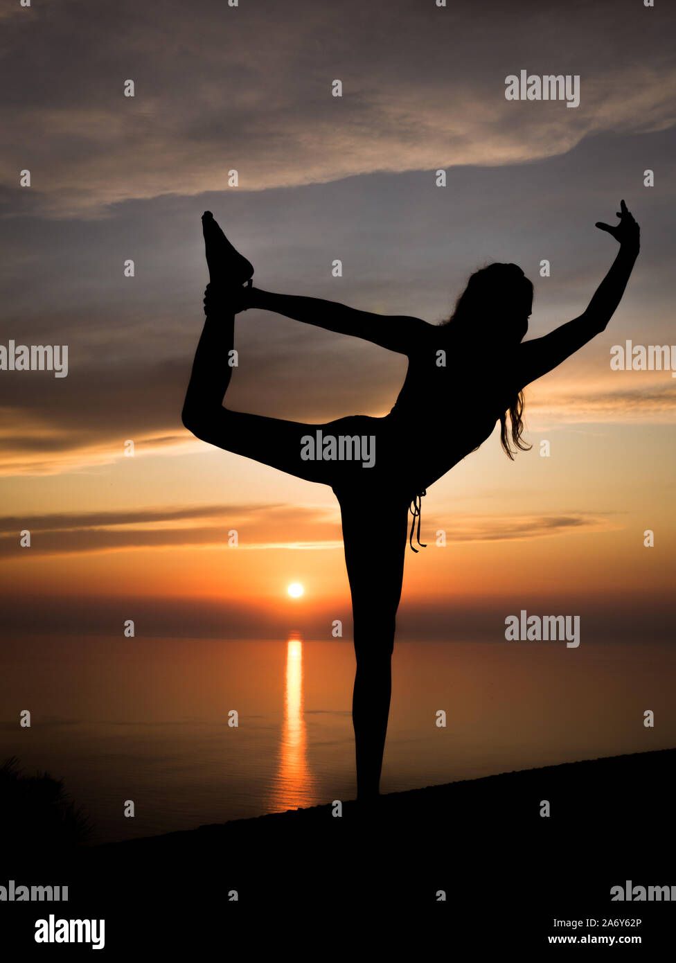 Silhouette di giovani e sportivi donna a praticare yoga (scala permanente di posa) con romantico tramonto e l'oceano in background in ora d'oro Foto Stock