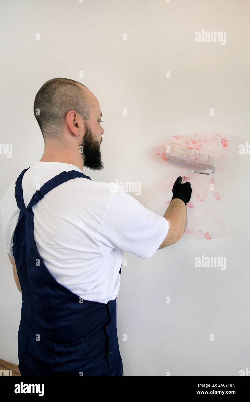 Operaio edile finitura facendo lavori di rinnovo nell'appartamento. Pittore professionista contraente utilizzando vernice bianca spazzola a rullo pittura della camera a parete. Foto Stock