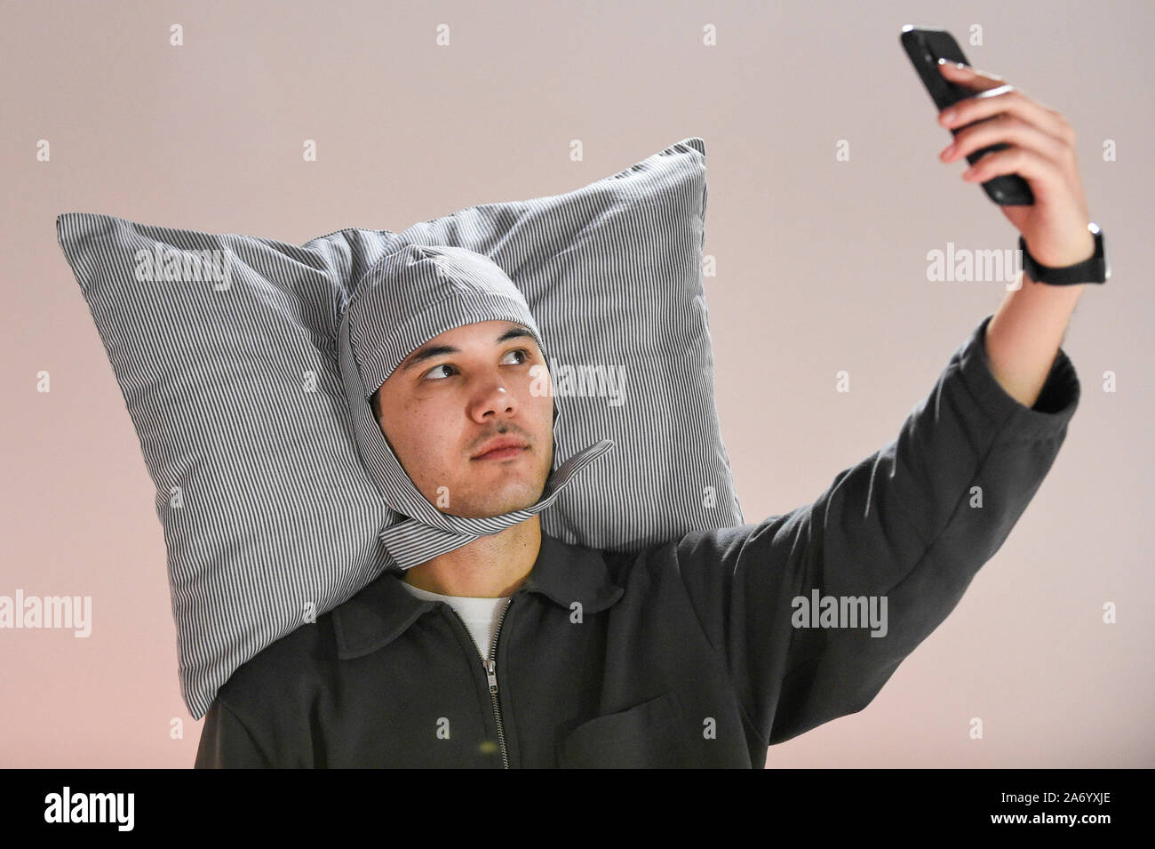 Londra, Regno Unito. Il 29 ottobre 2019. Un membro del personale indossa 'Pillowig', 2005 da JooYoun Paek, un design per consentire agli utenti di nap ovunque. Anteprima di '24/7: una chiamata di wake-up per il nostro mondo Non-Stop', una nuova apertura della mostra su 31 Ottobre presso la Somerset House. La mostra esamina la nostra incapacità di passare fuori dalla nostra cultura 24/7. Oltre 50 multi-disciplinare le opere esplorano la pressione per produrre e consumare le informazioni intorno all'orologio. prendendo i visitatori su un ciclo di 24 ore dall alba al tramonto attraverso installazioni interattive. Credito: Stephen Chung / Alamy Live News Foto Stock