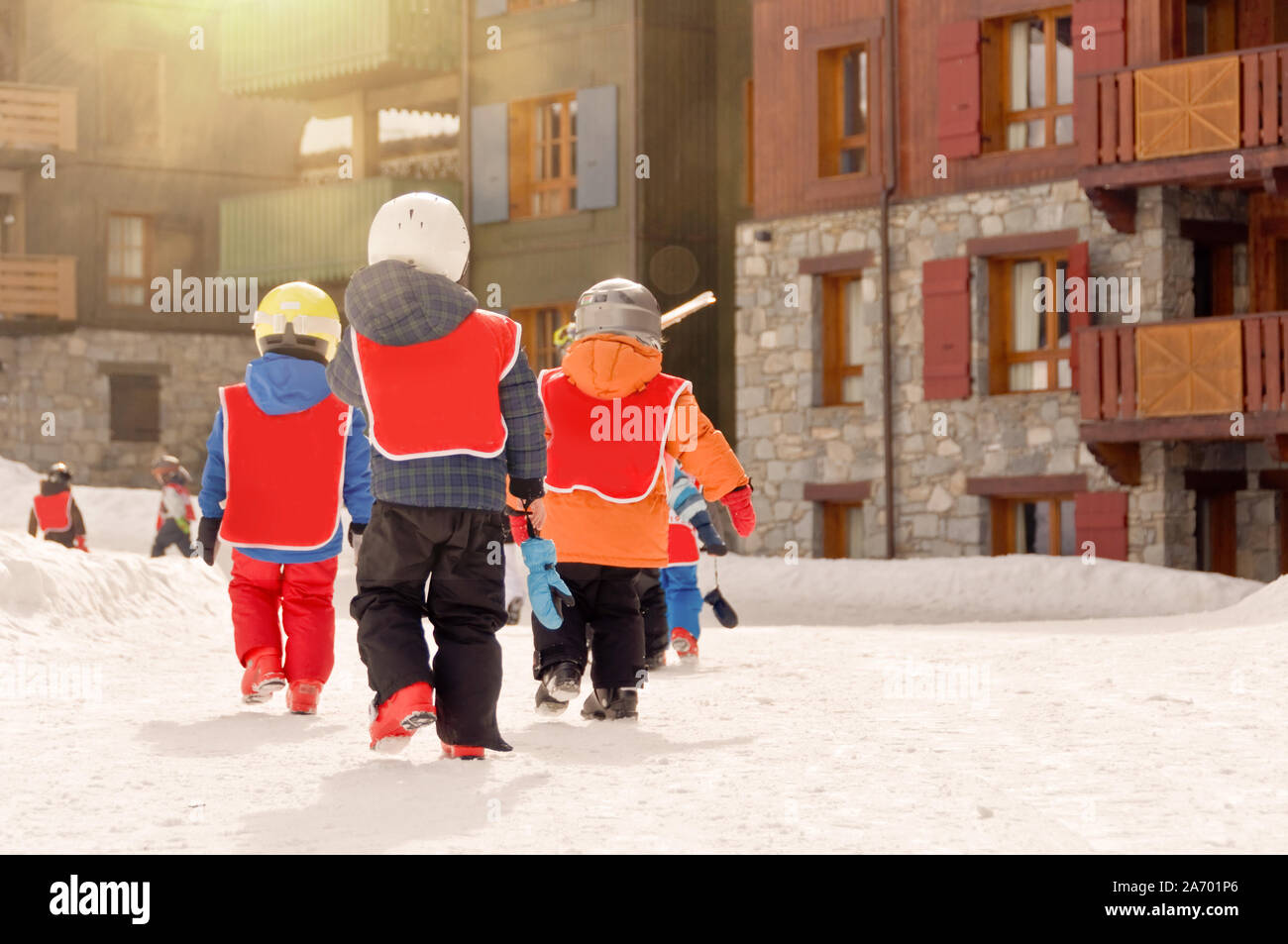 Un gruppo di giovani ragazzi tornare indietro a piedi per la stazione sciistica di villaggio dopo lezioni di sci, Alpi Francia Foto Stock