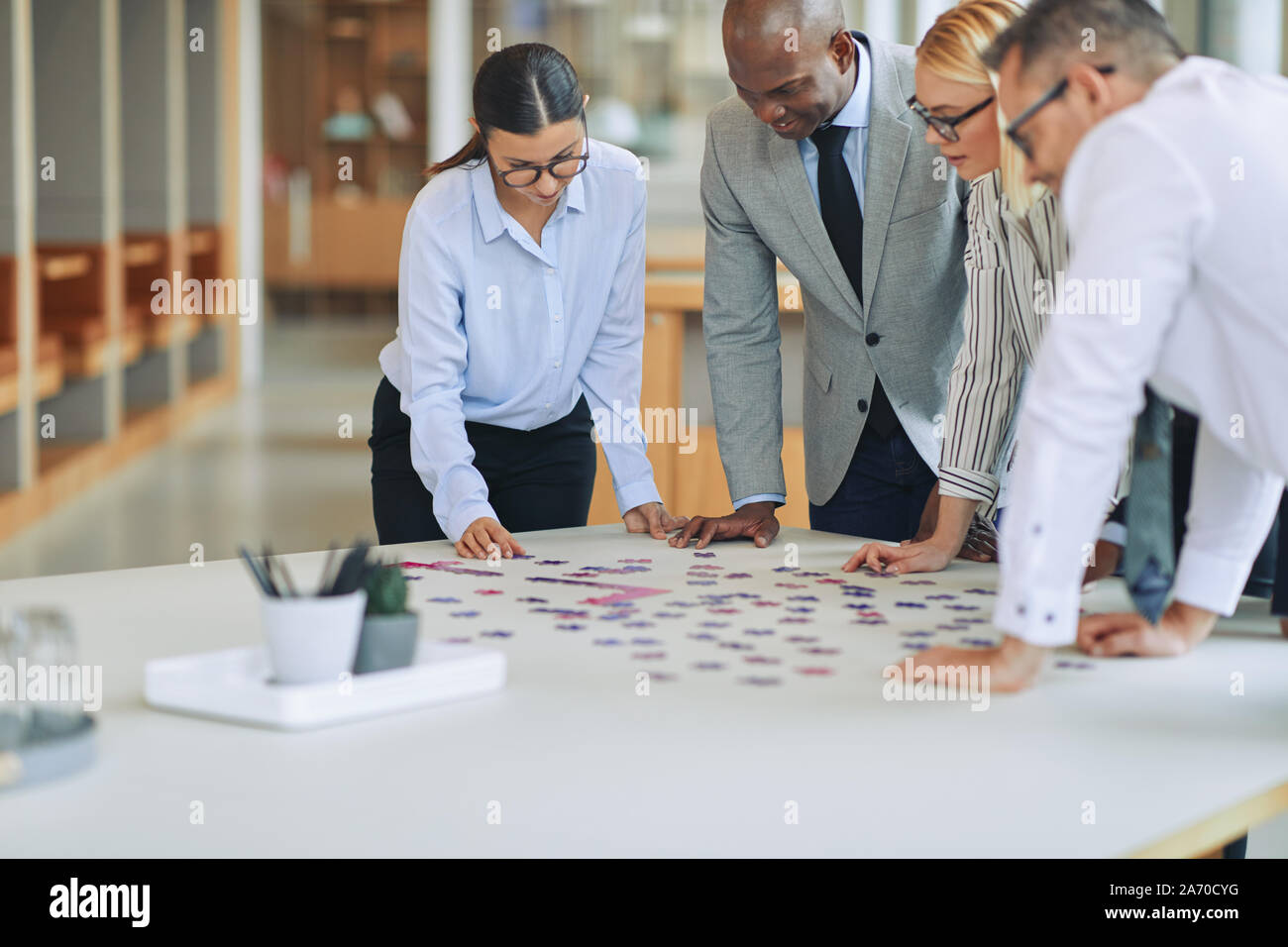 Gruppo di diversi imprenditori in piedi insieme attorno a un tavolo per riunioni in un ufficio focalizzato sul tentativo di risolvere un puzzle Foto Stock