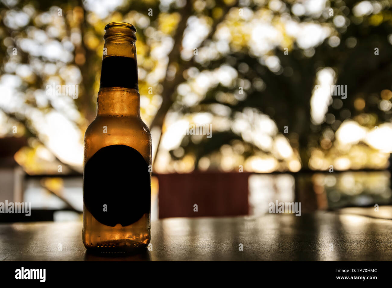 Bottiglia di birra sul tavolo con sfondo sfocato. La luce del tramonto. Foto Stock