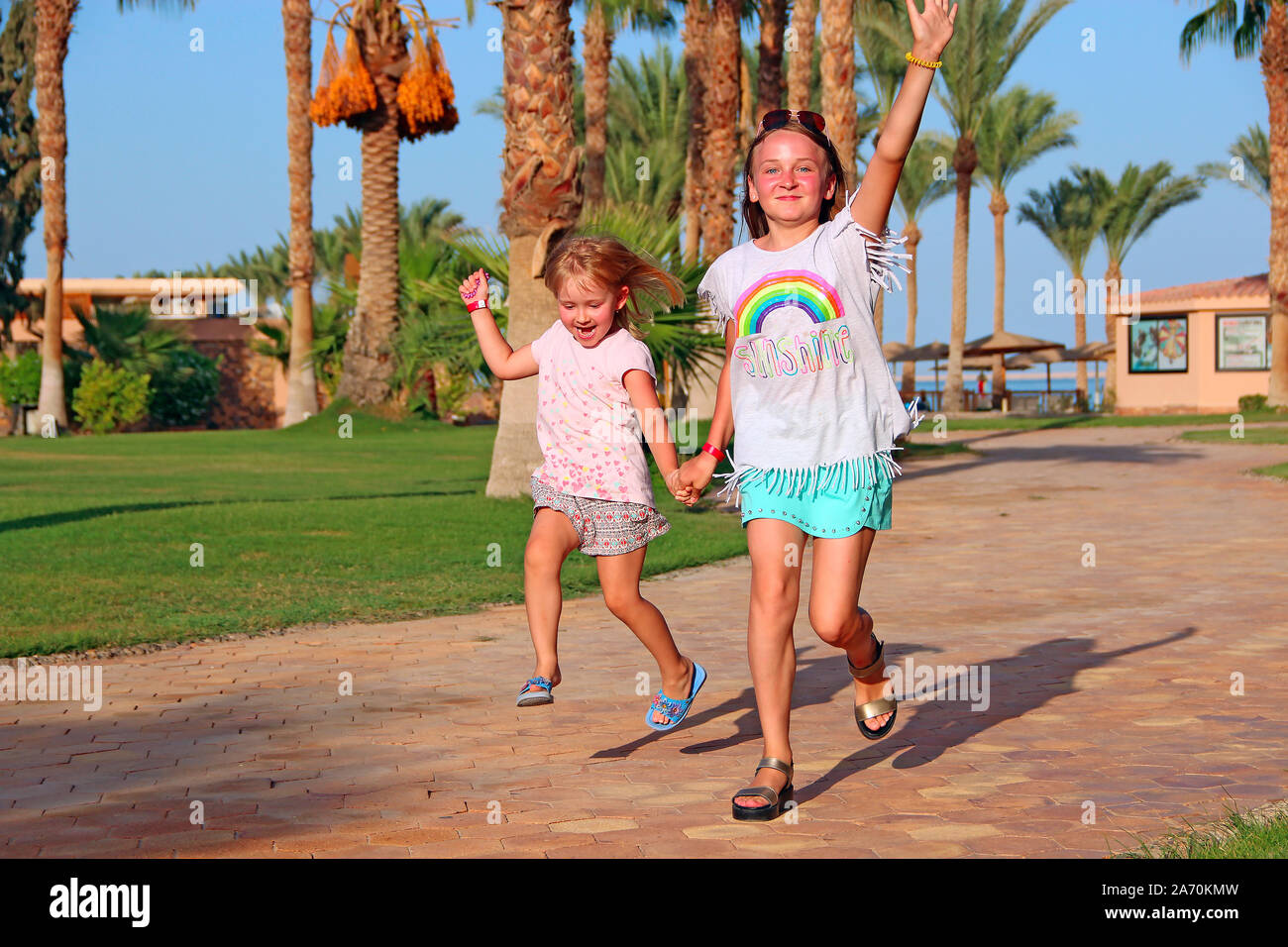 Felice team infantile divertendosi in esecuzione sul percorso nel tropico resort. La famiglia felice team. Sorelle godersi le vacanze estive. Le persone che si godono la vacanza con la famiglia Foto Stock