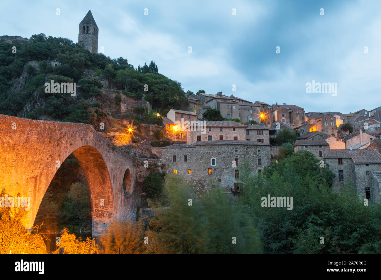Francia, Languedoc-Roussilon, Olargues, Pont du Diable bridge e la graziosa collina villaggio di olargues in montagna nera al tramonto. Foto Stock
