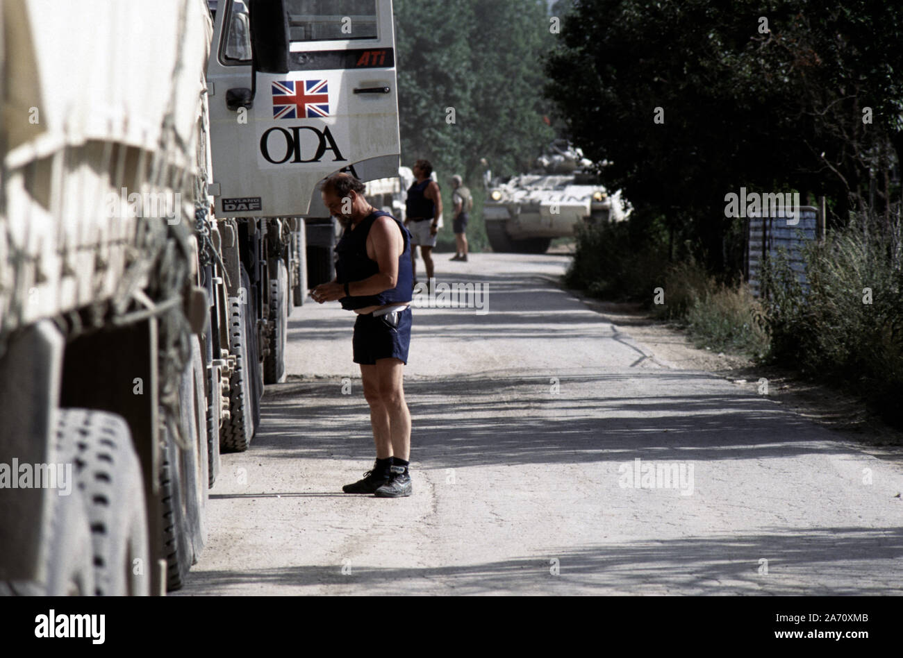 5 Luglio 1993 durante la guerra in Bosnia: sul percorso del diamante, un ODA (oltremare Developmant agenzia) convoglio di camion, assemblato appena a nord di Gornji Vakuf. Un camionista di indossare un giubbotto antiproiettile ha il tempo per una sigaretta come un esercito britannico Warrior approcci. Foto Stock
