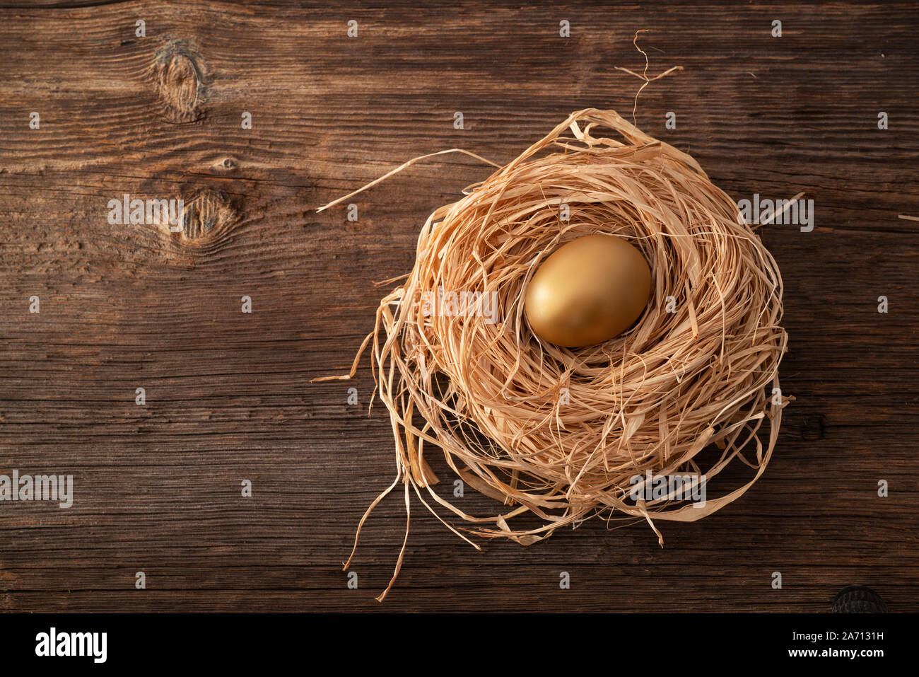 Unico e prezioso uovo dorato con nido su sfondo di legno Foto Stock