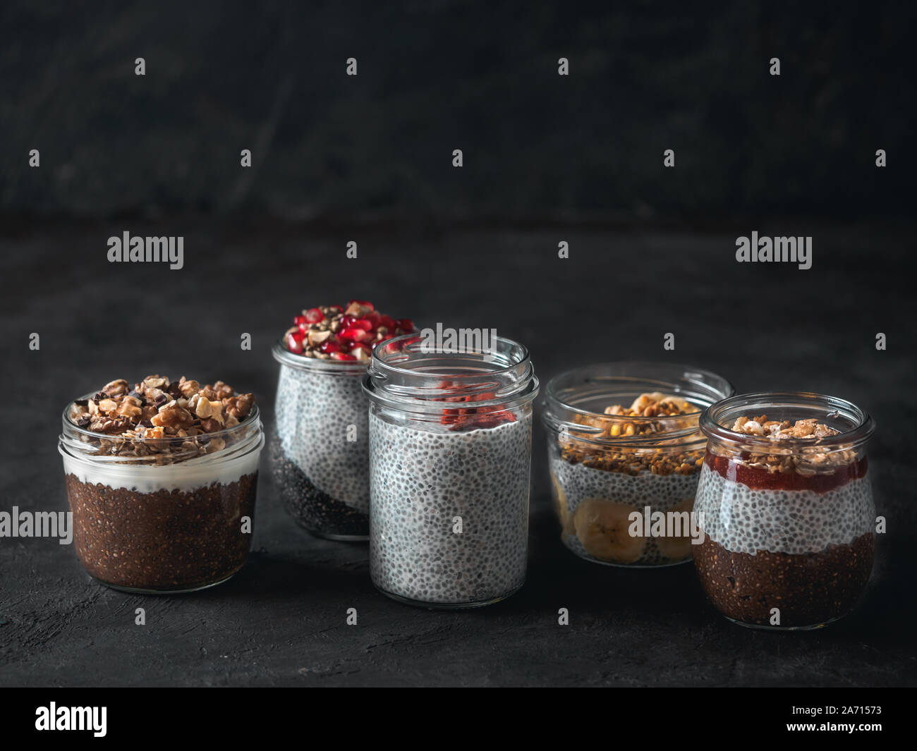 Set di chia pudding in differenti di vasetti di vetro scuro sul tavolo. Assortimento di chia puding con differenti di frutta,ingredienti. Copia spazio per il testo. Super,detox,sano pernottamento prima colazione concept Foto Stock