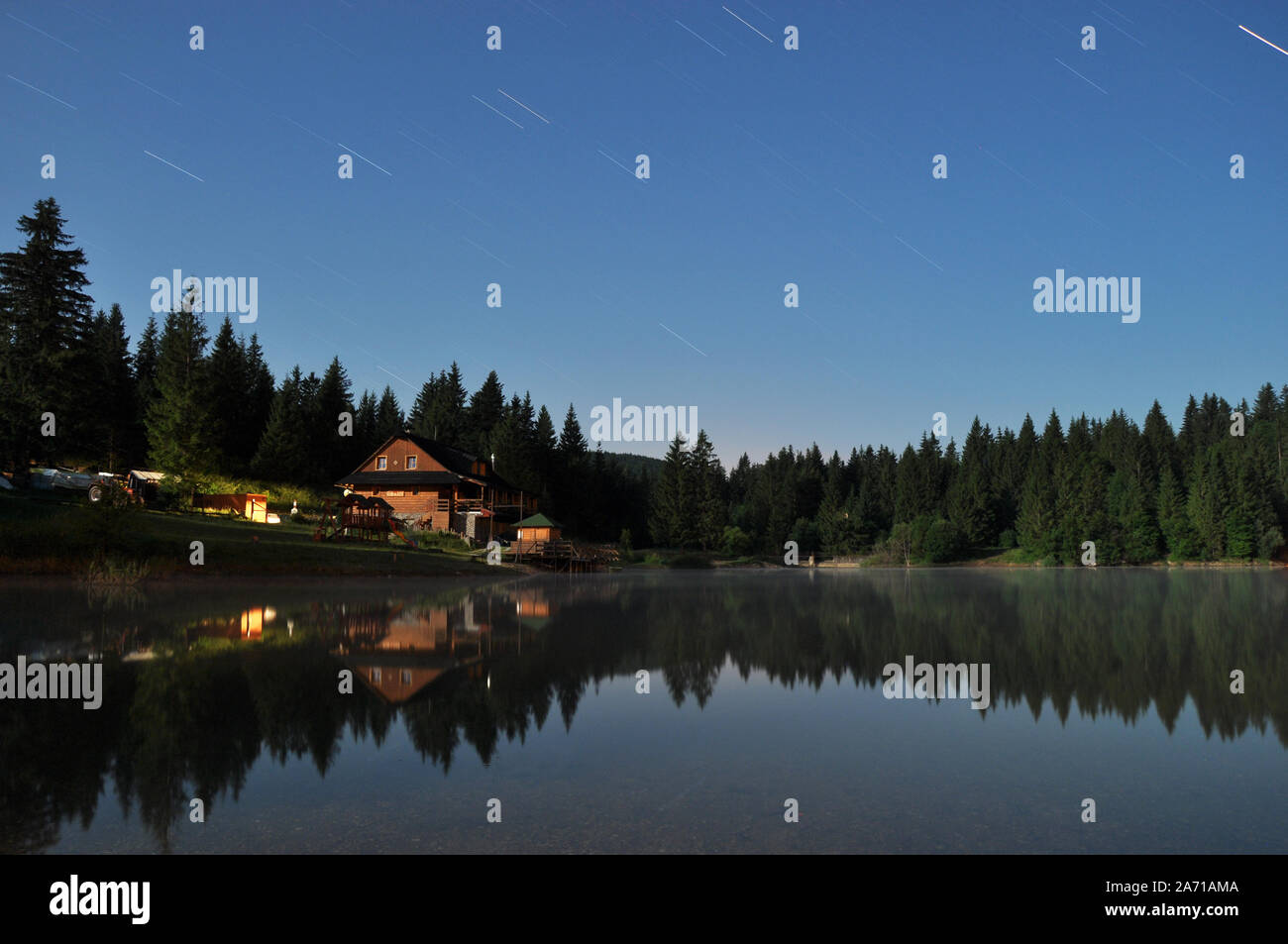 Foresta e cottage riflettente nel lago di notte Foto Stock
