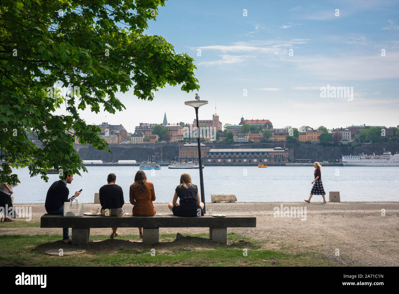 Persone mangiare il pranzo vista posteriore di un gruppo di giovani seduti su una panchina nel loro ora di pranzo, centrale di Stoccolma, Svezia. Foto Stock