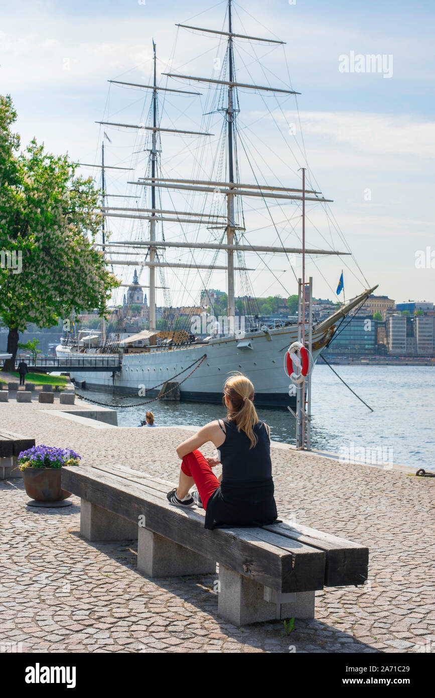 Concetto di giovane donna sola, vista posteriore in estate di una giovane donna seduta da sola su una panchina sul lungomare di Skeppsholmen, nel centro di Stoccolma, Svezia. Foto Stock