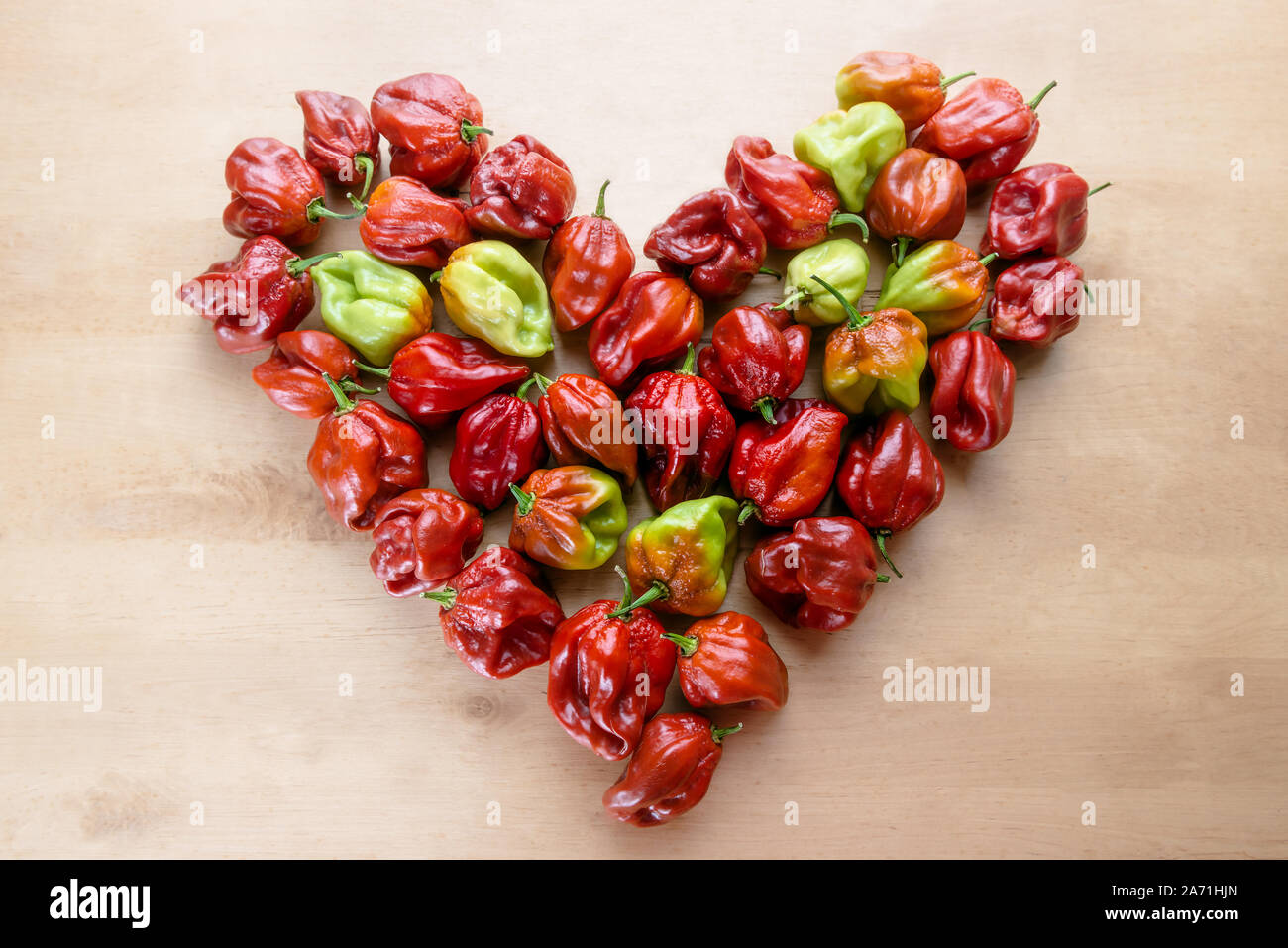 Red Hot Chili Pepper Scotch Bonnet Caraibi Antillais su sfondo di legno colorata nel cuore disegnato a forma di Foto Stock