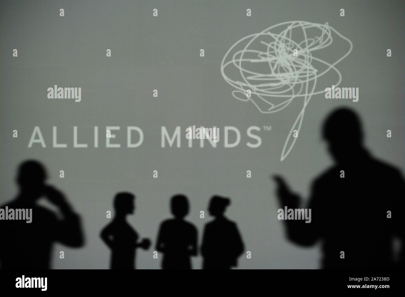 La Allied menti logo è visibile su uno schermo a LED in background mentre si profila una persona utilizza uno smartphone (solo uso editoriale) Foto Stock