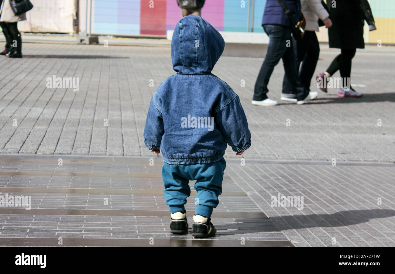 Il Toddler boy perso per strada. Indossando il denim giacca con cappuccio. Baby boy senza genitori,la strada affollata. Foto Stock