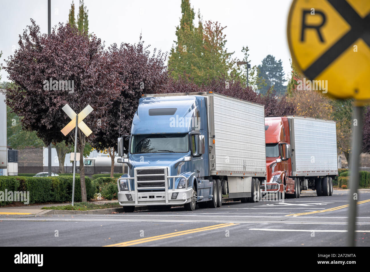 Big Rig cofano semi industriali Carrelli con griglia in alluminio di guardia e reefer semirimorchi in piedi su un incrocio ferroviario strada in una zona industriale wa Foto Stock