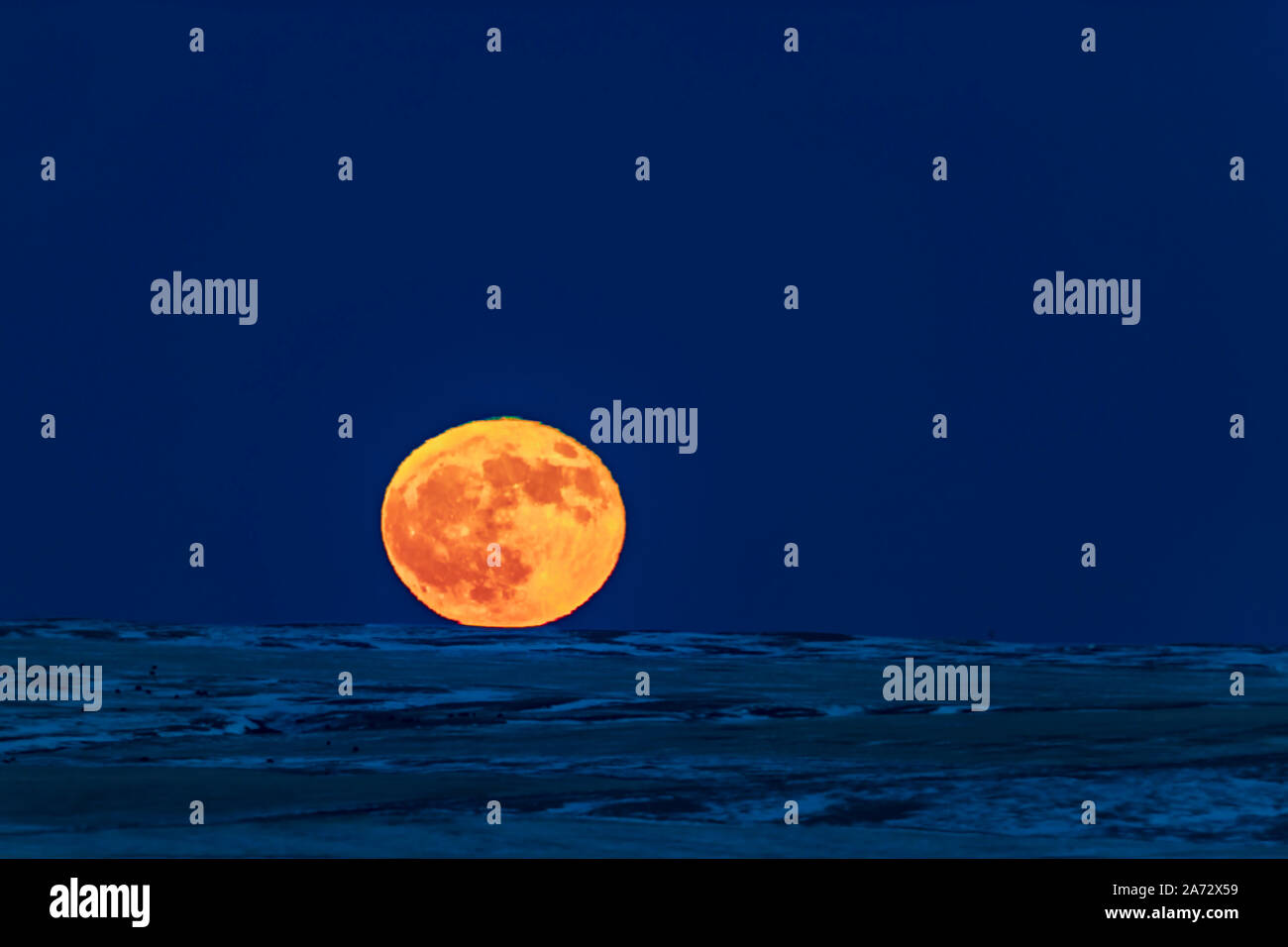 La luna piena sorge sul dicembre 22, 2018, il giorno dopo il solstizio d'inverno, in modo perfettamente chiaro cielo e oltre il lontano orizzonte per il nord-est Foto Stock