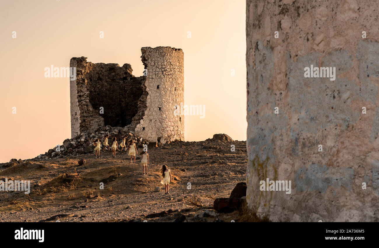 Bodrum, Turchia - 21 agosto 2019. Bambine in abiti di colore giallo a giocare intorno i famosi mulini a vento sulla cima della collina. Bodrum. Provincia di Mugla, Turke Foto Stock